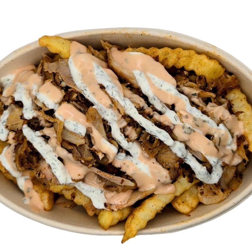 Waffle fries topped with gyro meat, white sauce, and a spicy orange sauce in a bowl.