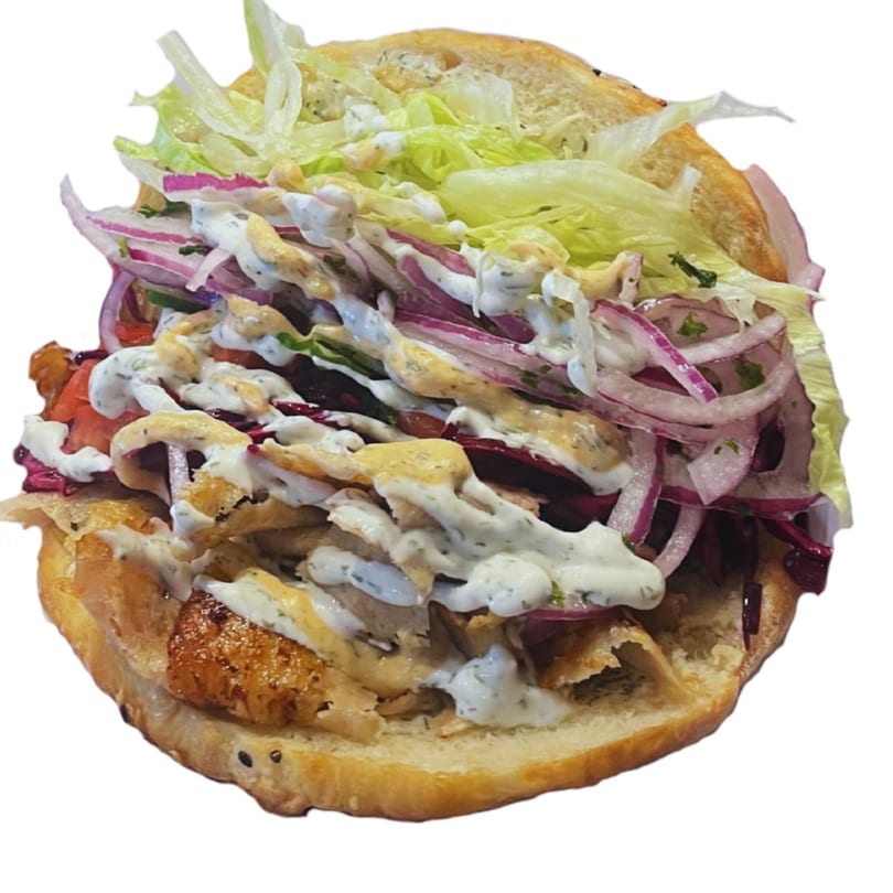 A close-up of a kebab with chicken, lettuce, red onions, and white and orange sauces.