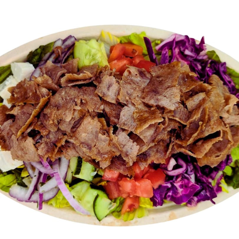 A close-up of a kebab salad with sliced meat, red cabbage, lettuce, tomatoes, and onions.